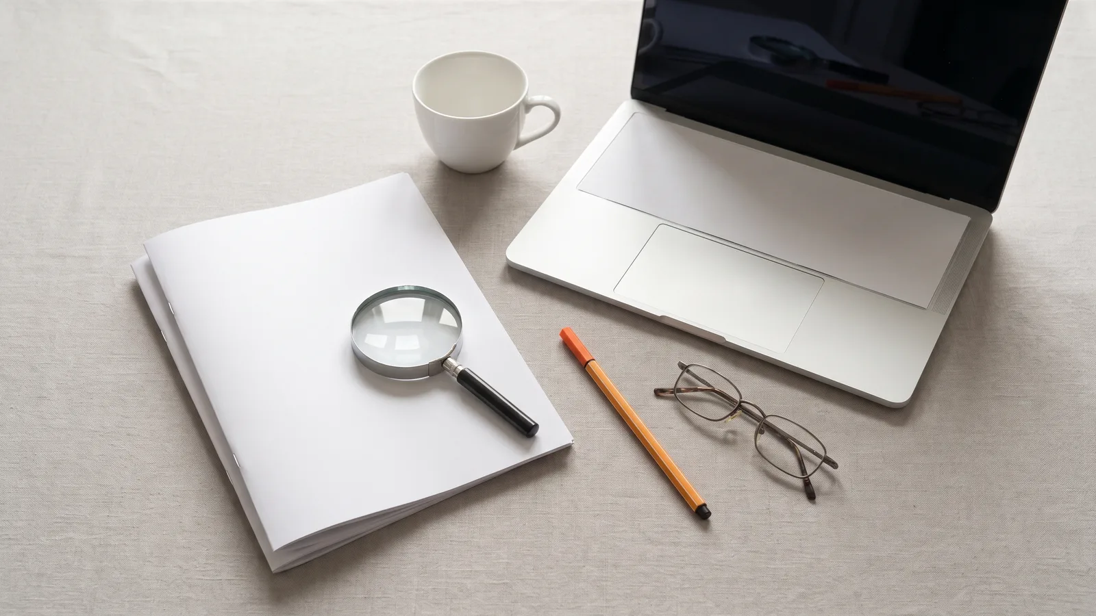 Blank stapled proposal under a magnifying glass beside a laptop, orange pen and glasses